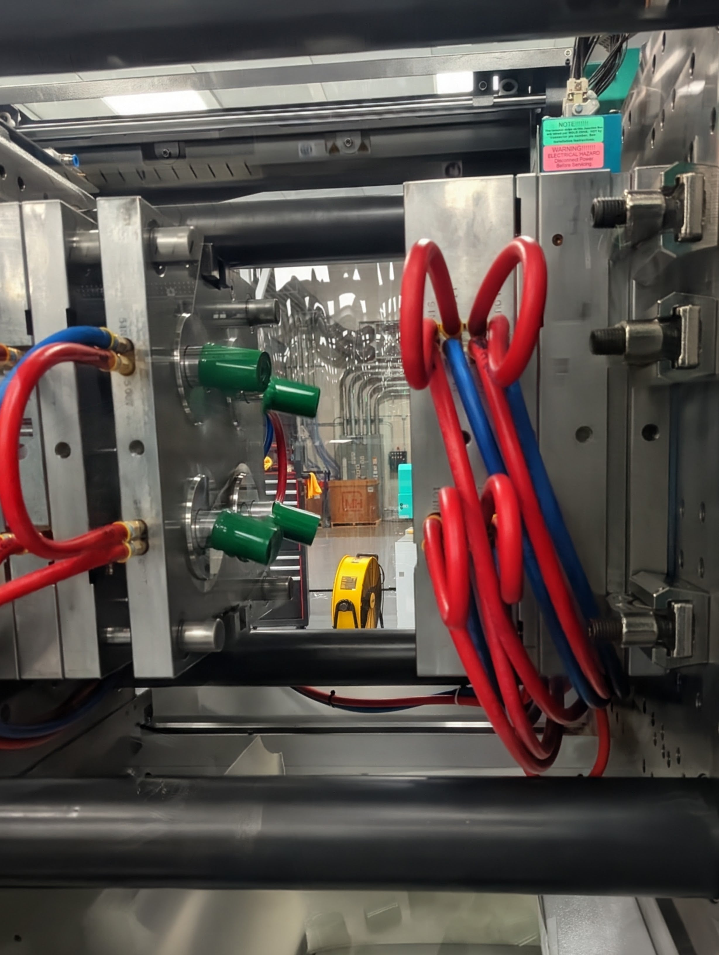 Close-up of industrial equipment making injection molded products with red and blue hoses and metal components.