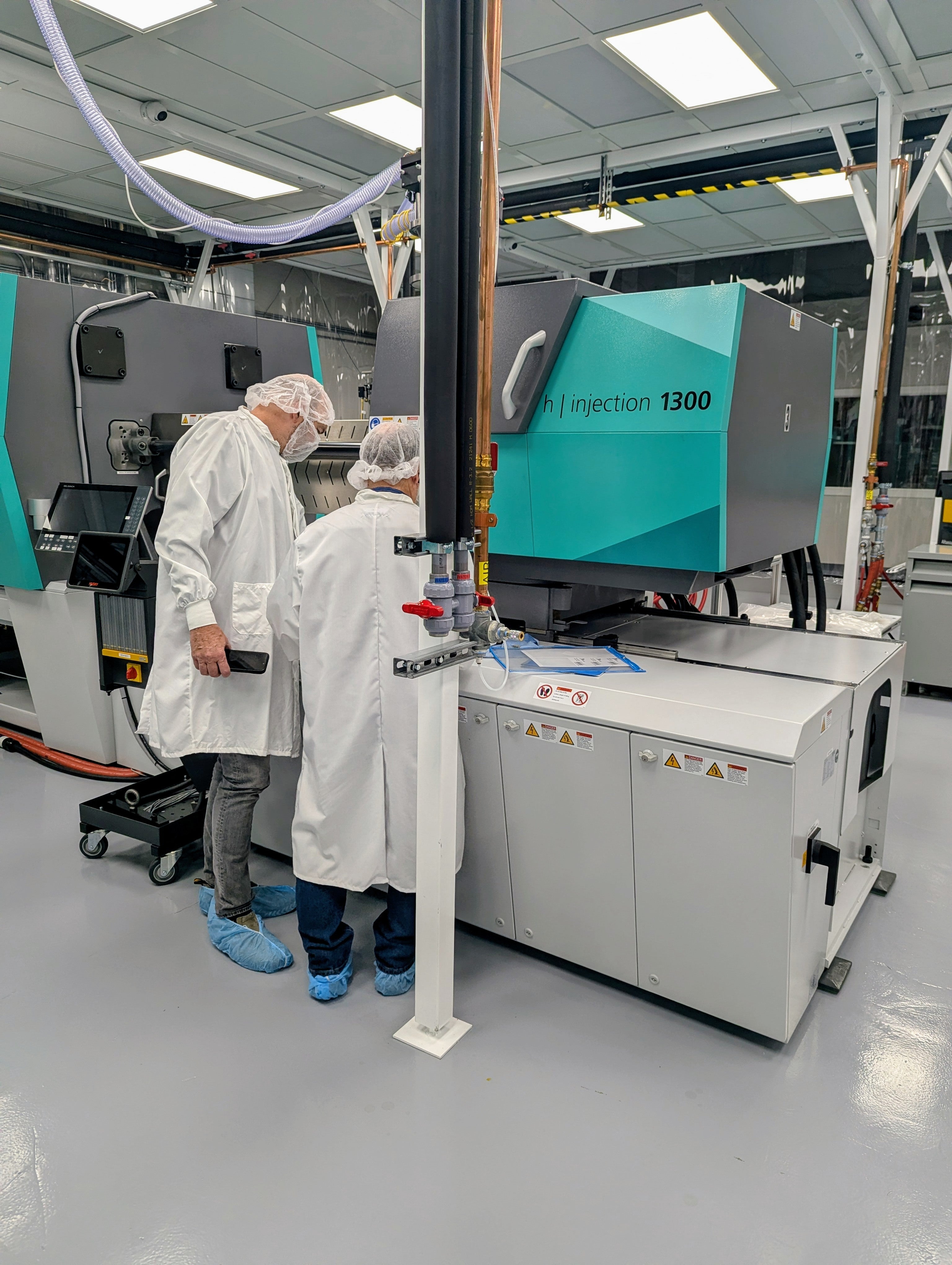 Two people wearing clean room attire standing next to large injection molding equipment